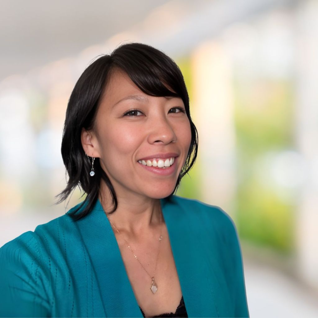 A headshot of Maya Ushikubo, founder of Spiral Roots Marketing. She's in a turquoise cardigan with a beautiful office in the background